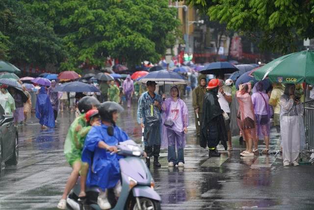 Nhiều người mặc áo mưa, cầm ô di chuyển, cố tìm cho mình một chỗ ngồi để đợi xem diễu binh A80. thaihoc2.jpg
