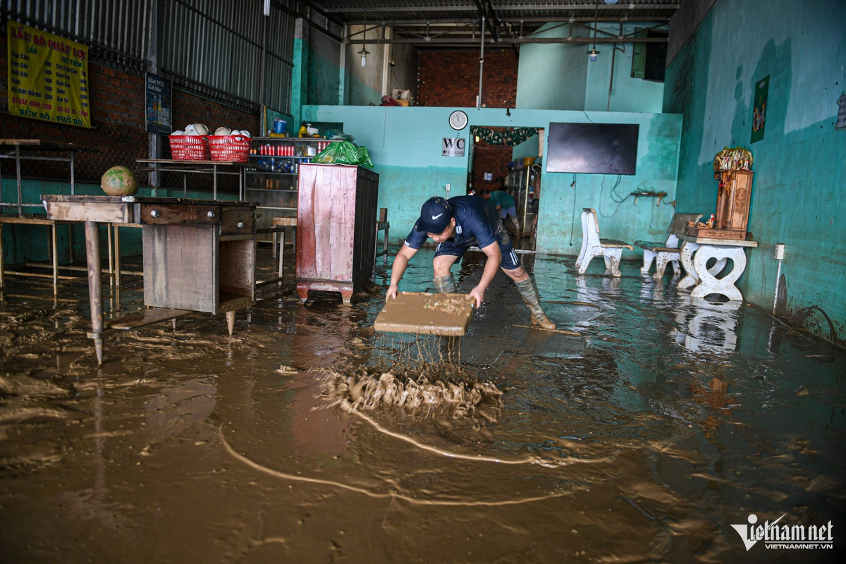 Anh Đặng Văn Khánh dùng bìa xốp đẩy bùn trên sàn, ngán ngẩm không biết nên bắt đầu dọn từ đâu. Đồ đạc hư hỏng gần hết, nhiều vật dụng bị cuốn trôi hoặc bám đầy bùn. Gia đình anh kinh doanh quán ăn, nên bàn ghế, nồi niêu và các vật dụng đều bị ngập, hầu như không còn gì nguyên vẹn.