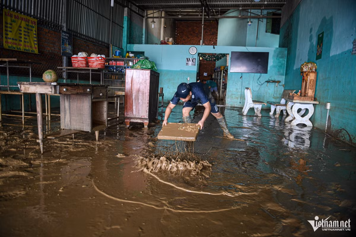 Anh Đặng Văn Khánh dùng bìa xốp đẩy bùn trên sàn, ngán ngẩm không biết nên bắt đầu dọn từ đâu. Đồ đạc hư hỏng gần hết, nhiều vật dụng bị cuốn trôi hoặc bám đầy bùn. Gia đình anh kinh doanh quán ăn, nên bàn ghế, nồi niêu và các vật dụng đều bị ngập, hầu như không còn gì nguyên vẹn.