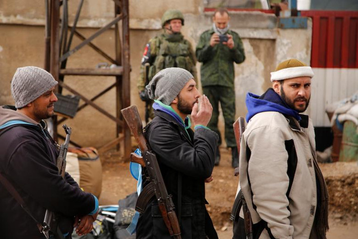 Binh sĩ Nga đứng quan sát các chiến binh nổi dậy Syria xếp hàng chờ được đưa ra khỏi quận Waer ở tỉnh Homs hồi tháng 3/2017, sau khi quân nổi dậy và lực lượng chính phủ Damascus đạt được một thỏa thuận.