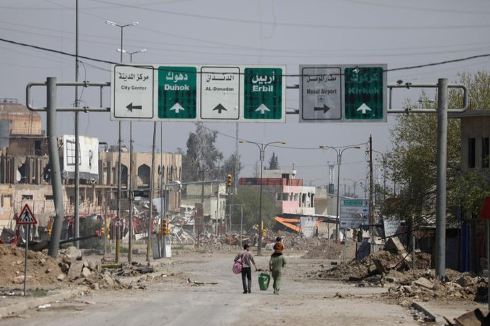 Người dân mang theo đồ đạc đi bộ trên một con đường ở khu vực do lực lượng Iraq kiểm soát tại thành phố lớn thứ hai Iraq.