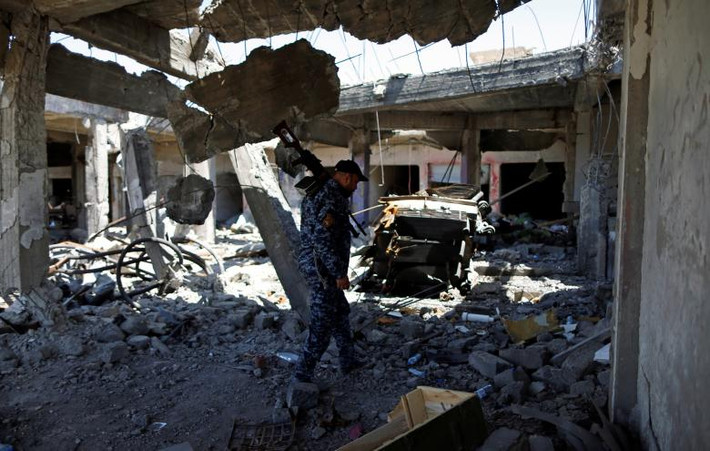 Một cảnh sát Iraq đi qua tòa nhà đổ nát ở Tây Mosul ngày 26/4.