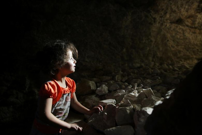 Một bé gái ngồi trong hang trú ẩn dưới lòng đất ở Idlib.