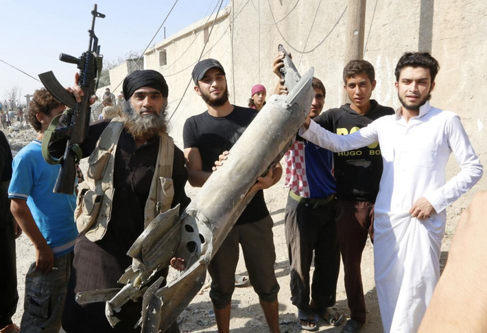 Một chiến binh IS (trái) cầm mảnh vỡ của một chiếc đấu cơ Syria bị rơi ở Raqqa hôm 16/9/2014.