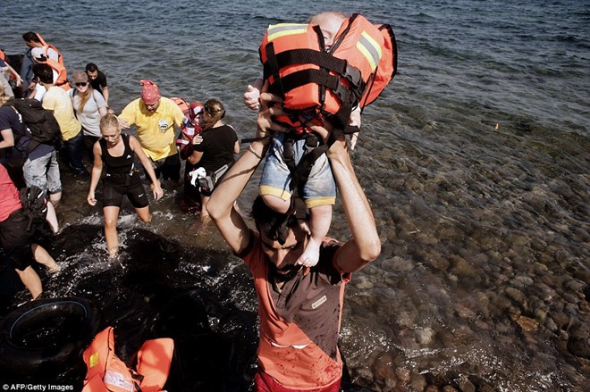 Một người đàn ông Syria bế bé trai đeo áo phao khi nhóm người của họ vừa đến đảo Lesbos. Liên Hiệp Quốc cho biết tình hình nội chiến ở Syria khiến cuộc sống trở nên tồi tệ, buộc khoảng 4 triệu người rời khỏi đất nước để di cư sang các quốc gia khác. Ngày 20/9, Ngoại trưởng Mỹ John Kerry cho biết Mỹ sẽ tiếp nhận 85.000 người tị nạn trong hai năm tới để chia sẻ gánh nặng với châu Âu.