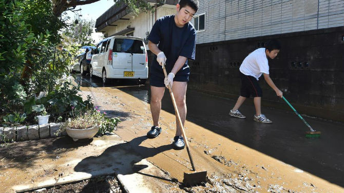 Các thanh niên dọn con đường đầy bùn bên ngoài nhà của họ ở thành phố Joso, tỉnh Ibaraki.