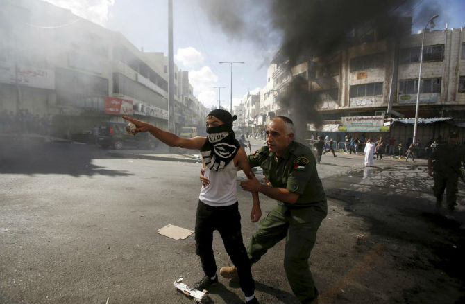 Một nhân viên an ninh Palestine cố ngăn cản một thanh niên ném đá vào binh sĩ Israel khi căng thẳng gia tăng tại thánh đường al-Aqsa, Jerusalem.