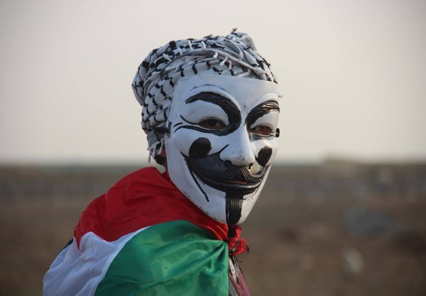 Một người Palestine đeo mặt nạ khi tham gia biểu tình. Ảnh: FNA.