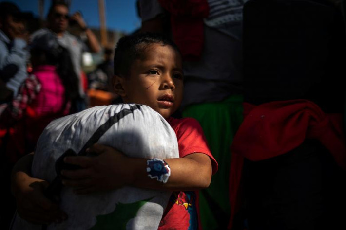 Một bé trai ôm túi đồ đứng gần hàng rào biên giới Mỹ-Mexico ở Tijuana, Mexico, ngày 15/11.
