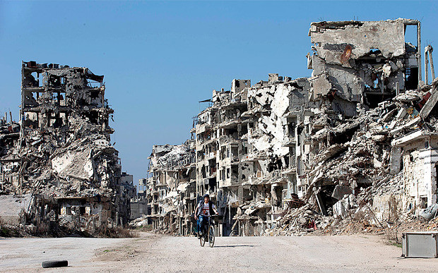 Người dân Syria đạp xe trên con đường ở Homs. Hai bên đường là những tòa nhà đã bị chiến tranh tàn phá. Sẽ mất nhiều năm để tái thiết thành phố của quốc gia Trung Đông này.