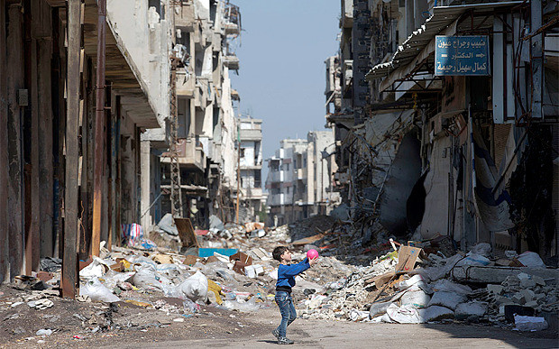 Bé trai Syria chơi đùa với quả bóng giữa cảnh đổ nát ở Homs.
