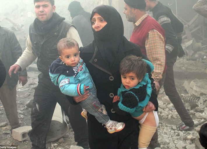 Người phụ nữ bế theo hai đứa trẻ sơ tán khỏi khu vực vừa bị ném bom ở Aleppo ngày 15/12/2013.