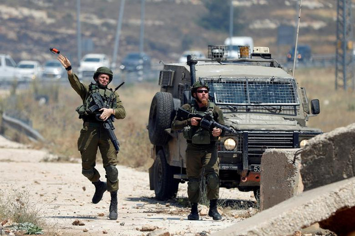 Một binh sĩ Israel ném lựu đạn về phía người biểu tình Palestine gần khu định cư Do Thái Beit El ở Bờ Tây ngày 24/6. Ảnh: Reuters.