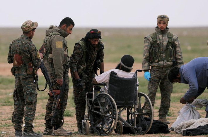 Các thành viên SDF hỏi thăm một người đàn ông ngồi xe lăn gần ngôi làng Baghouz ngày 27/2.