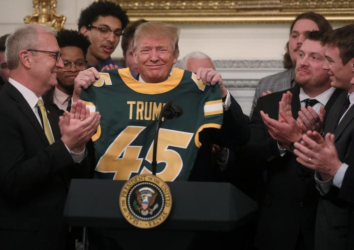 Tổng thống Trump cầm chiếc áo có in tên của ông tại buổi tiệc.