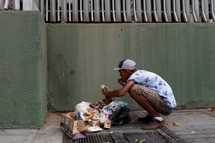 Một thanh niên đang ngồi ăn cạnh đống rác ở Caracas ngày 27/2.