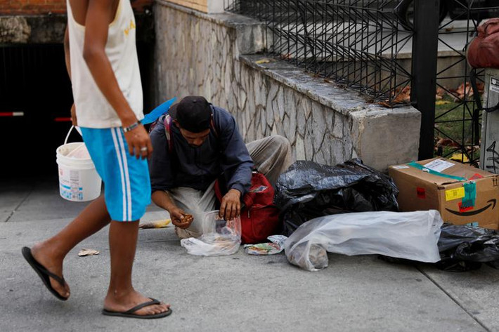 Một người đàn ông tìm đồ ăn trong túi rác trên đường phố Caracas.