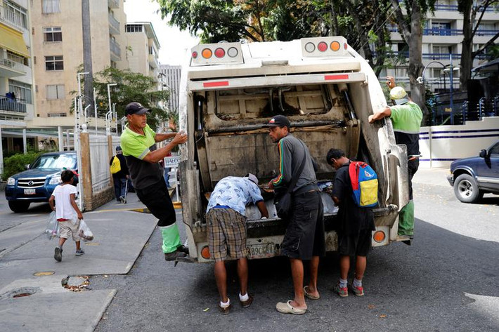 Những đứa trẻ tìm đồ ăn phía sau xe tải chở rác ở Caracas hôm 27/2.