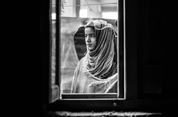 Insha, 10 tuổi, nhìn ra ngoài cửa sổ ở làng Dialgam, huyện Anantnag, cách thành phố Srinagar khoảng 55 km về phía nam. Cha của Insha thiệt mạng trong một vụ tấn công ở Anantnag vào năm 2015.