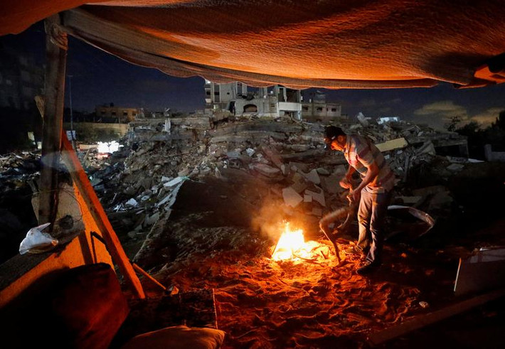 Người đàn ông Palestine đốt lửa trong túp lều tạm bợ vào buổi tối.