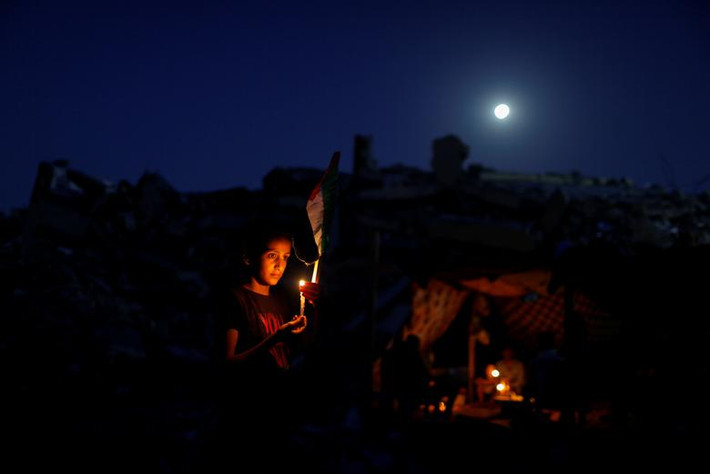 Một thành viên trong gia đình Zawaraa người Palestine cầm nến gần túp lều tạm bợ được dựng giữa đống đổ nát của ngôi nhà bị phá hủy trong đợt không kích của Israel, tại Gaza ngày 25/5.