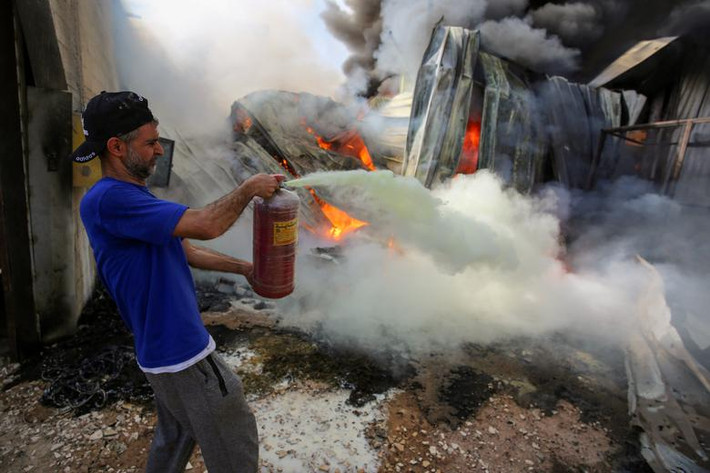 Một người đàn ông Palestine dập lửa tại một nhà máy sau khi nó bị trúng đạn pháo của Israel, tại Dải Gaza ngày 17/5.