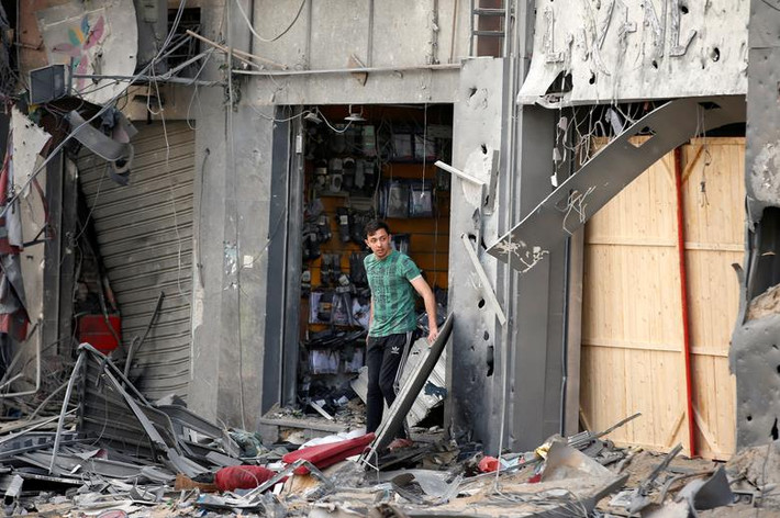 Người đàn ông Palestine đứng bên ngoài một cửa hàng bị hư hại sau vụ không kích của Israel nhằm vào thành phố Gaza hôm 13/5.