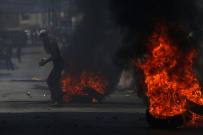 Một người biểu tình Palestine đứng cạnh đống lốp xe đang bốc cháy trong cuộc đụng độ với binh sĩ Israel gần trạm kiểm soát Qalandiya gần thành phố Ramallah, Bờ Tây, ngày 21/7/2017. (Nguồn ảnh: Reuters)