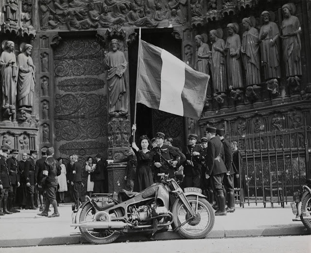 Cô gái Pháp vẫy cờ chào mừng các lực lượng giải phóng thủ đô Paris khi họ diễu hành qua nhà thờ Đức Bà Paris ngày 26/8/1944. Ảnh: VT.