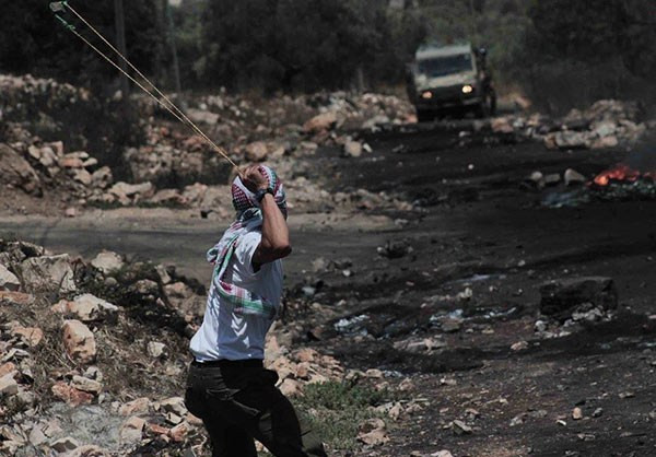 Một thanh niên Palestine ném đá về phía binh sĩ Israel ở làng Kufr Qadoom hôm 30/6. Ảnh: FNA.