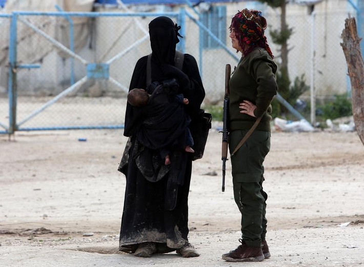 Một nữ chiến binh thuộc Lực lượng Dân chủ Syria (SDF) đứng cạnh vợ của một tay súng IS tại khu trại al-Hol ở Hasaka.