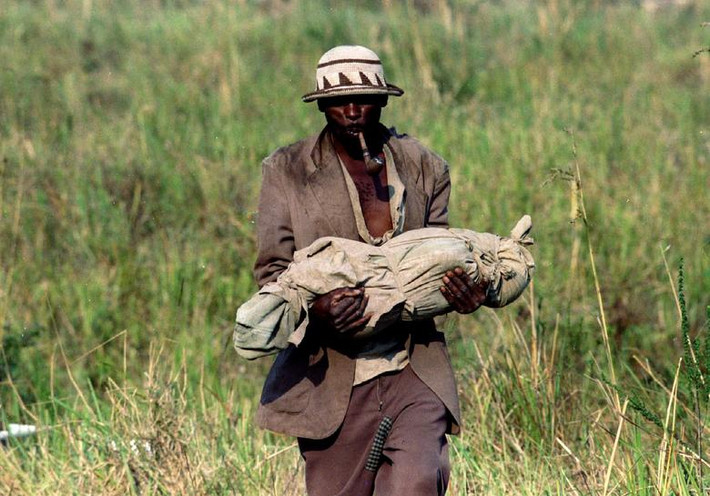 Một người tị nạn Rwanda bế một thi thể đi qua cánh đồng để tới ngôi mộ tập thể ngày 29/7/1994.