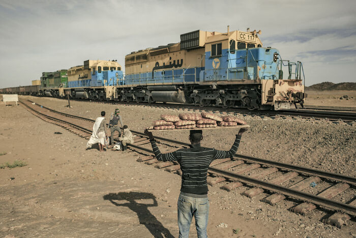 Chuyến tàu chở quặng sắt Mauritania chạy xuyên sa mạc Sahara là một trong những đoàn tàu dài nhất thế giới. Ảnh: Một số người chờ lên chuyến tàu nguy hiểm nhất thế giới này tại thị trấn Choum trong khi một thanh niên đội bánh mì trên đầu để bán cho hành khách. (Nguồn ảnh: BP)