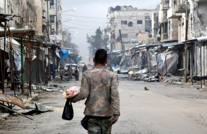 Một binh sĩ Syria mang theo đồ ăn đi bộ trên con đường ở Maarat al-Numan.