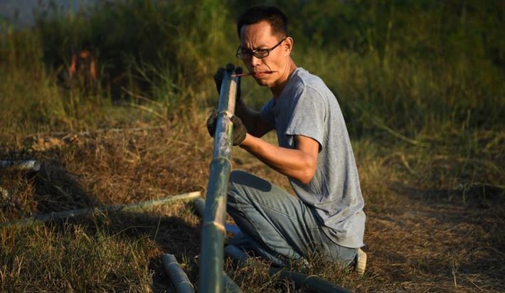 Da Wang đang làm một cái giá đỡ bằng tre trong trang trại của mình.