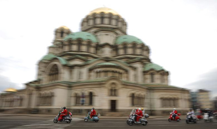 Các thành viên của câu lạc bộ Vespa mặc trang phục ông già Noel đi qua nhà thờ Alexander Nevski ở Sofia, Bulgaria, hôm 21/12.