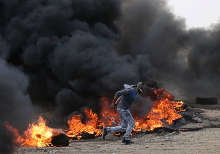 Một người biểu tình Palestine chạy qua đống lửa đỏ rực trong cuộc đụng độ với lực lượng Israel gần biên giới Gaza-Israel ngày 14/5. Ảnh: Yahoo News.