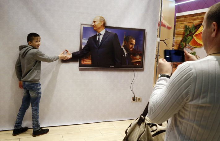 Một thiếu niên chụp hình với một tấm áp phích in hình Tổng thống Nga Vladimir Putin và cựu tổng thống Mỹ Barack Obama tại một trung tâm mua sắm ở St. Petersburg năm 2016. Đối với nhiều doanh nghiệp Nga, gương mặt của ông chủ Điện Kremlin mang đến cho họ cơ hội vàng về kinh doanh. "Thương hiệu Putin" được họ tìm cách tận dụng triệt để.
