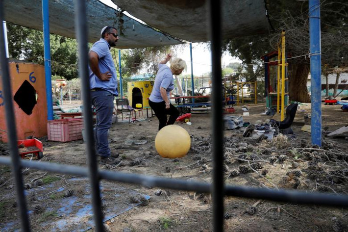 Mọi người dọn dẹp đống đổ nát trên sân trường mẫu giáo ở Kibbutz phía Israel trên biên giới Israel-Gaza.