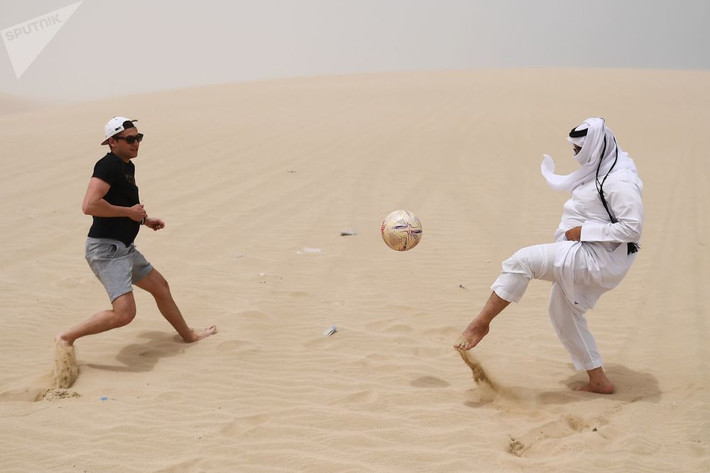 Hai người đàn ông chơi đá bóng trên sa mạc Khor Al Adaid, thủ đô Doha, Qatar.
