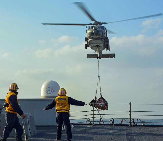 Hai nhân viên hướng dẫn trực thăng MH-60R tiếp tế nhu yếu phẩm cho tàu khu trục USS Lassen (DDG-82) trong một nhiệm vụ trên biển Hoa Đông.