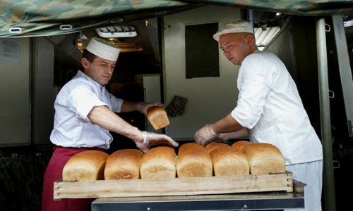 Hai nhân viên nhà bếp sắp bánh mì vừa nướng xong ra khay để chuẩn bị bữa ăn cho các phi công Nga.