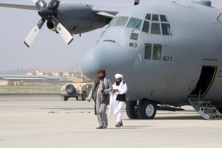 Hai chiến binh Taliban đi phía trước một chiếc máy bay quân sự tại sân bay Hamid Karzai ngày 31/8.
