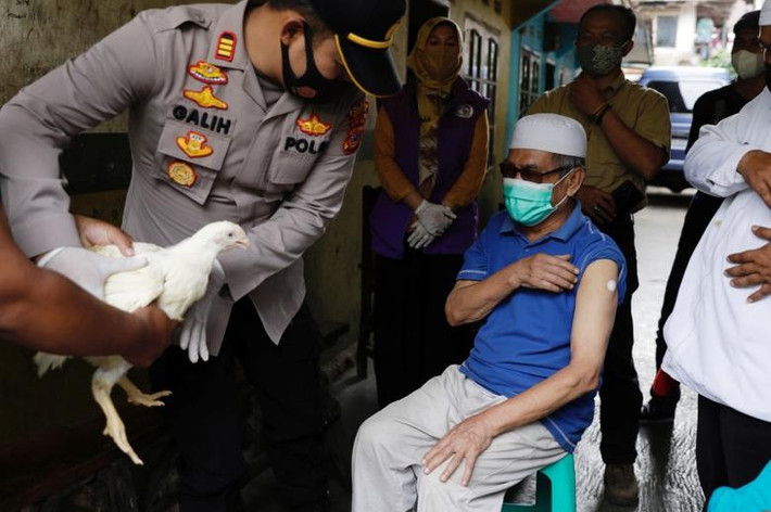 Cảnh sát trưởng Galih Apria tặng một con gà cho Jeje Jaenudin, 68 tuổi ở làng Sindanglaya, Tây Java, ngày 15/6, sau khi ông được tiêm mũi vắc xin đầu tiên. Ảnh: Reuters.