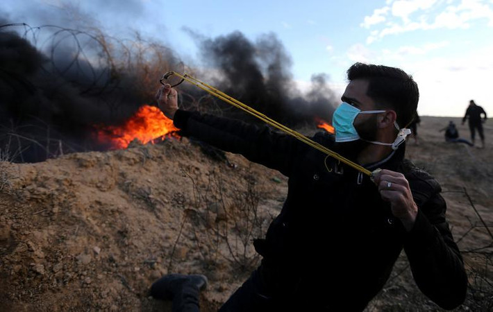 Một người biểu tình Palestine bắn đá về phía lực lượng an ninh Israel gần khu vực biên giới với Israel ở phía nam Dải Gaza khi người dân Palestine kêu gọi biểu tình “Ngày giận giữ” nhằm phản đối quyết định của Tổng thống Trump về Jerusalem, ngày 26/1.