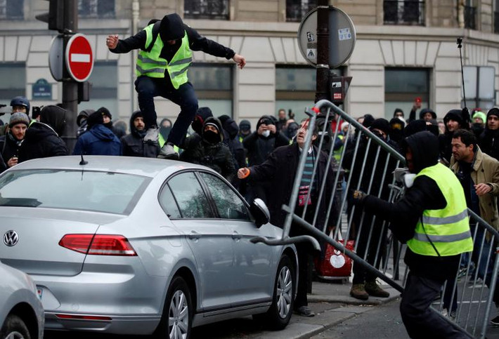 Người biểu tình bịt mặt nhảy lên một chiếc ô tô trong cuộc biểu tình ở Paris.