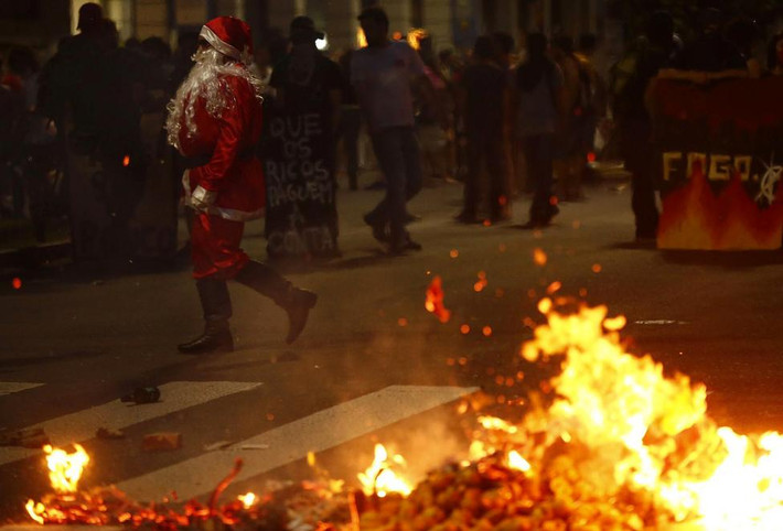 Một người biểu tình hóa trang thành ông già Noel đi qua đám cháy trên đường phố ở Porto Alegre, ngày 13/12.