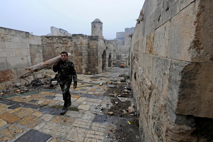Một thành viên của lực lượng trung thành với chính phủ Syria vác khúc gỗ đi bộ trong khu vực Thành cổ Aleppo hôm 13/12.