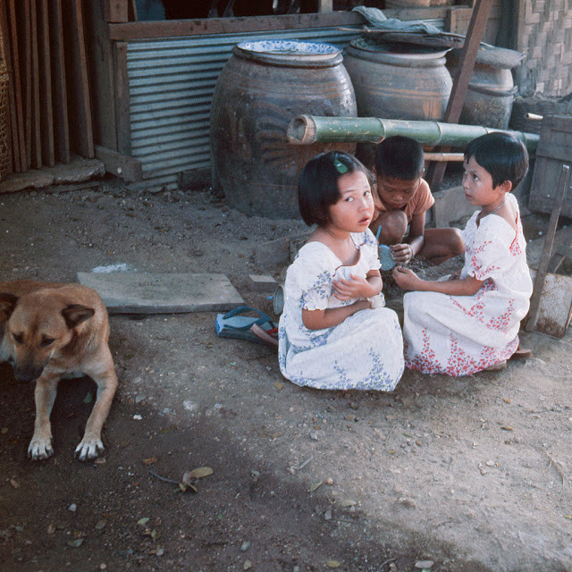 Các em nhỏ ngồi túm tụm trước nhà trong bức ảnh chụp hồi cuối thập niên 1970.