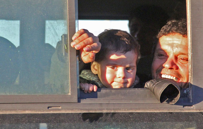 Một bé trai ngồi cùng cha nhìn ra ngoài cửa sổ xe buýt khi tới Khan-al-Aassal, phía tây thành phố Aleppo, trong hành trình tới Idlib. (Nguồn ảnh: Daily Mail)